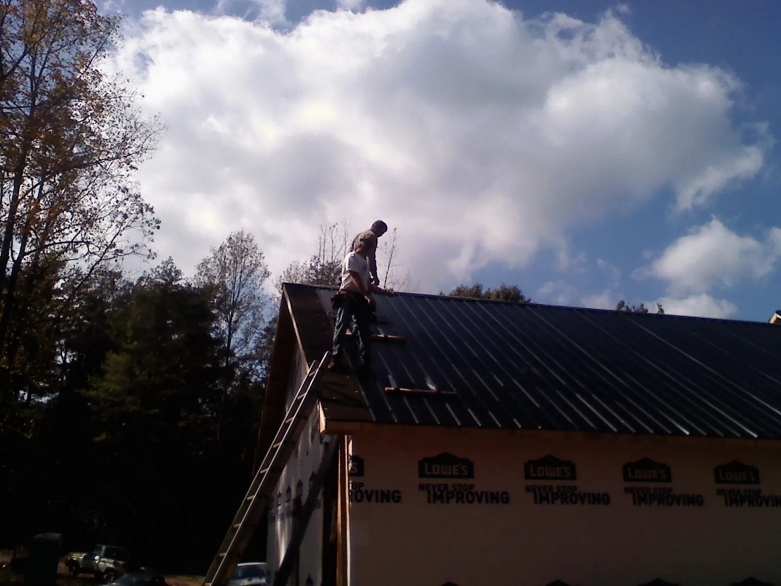 Roofer fastening dark metal panels high against a cloudy sky, from a Roof Inspection job in New Windsor