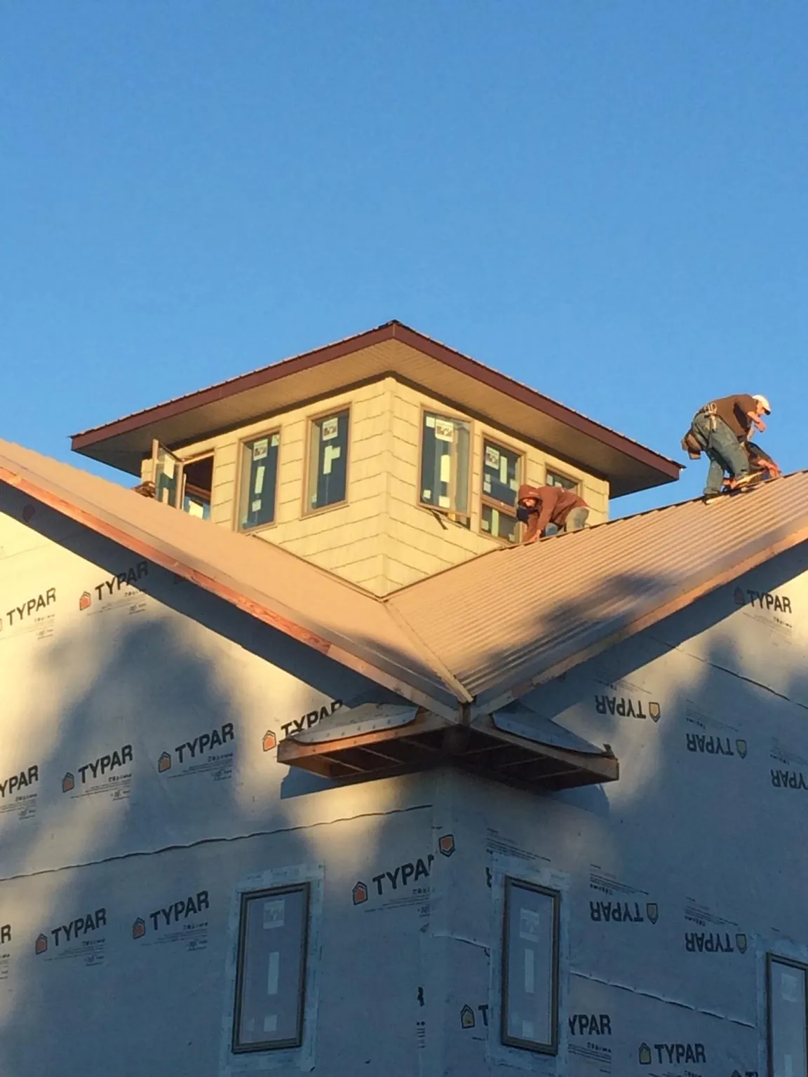 Roofers working around a rooftop cupola on a new metal roof at sunset in New Windsor